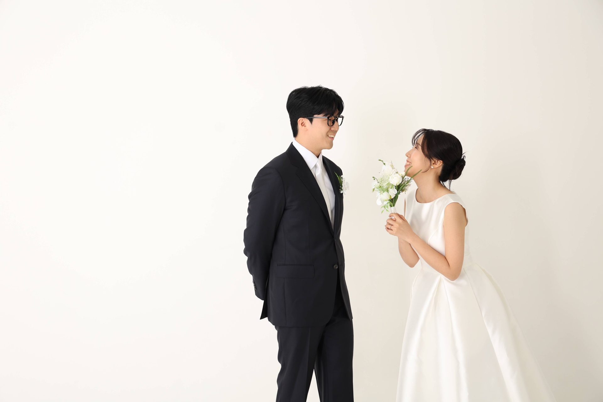 흰 배경 앞에서 꽃다발을 사이에 두고 마주 보는 두 사람
